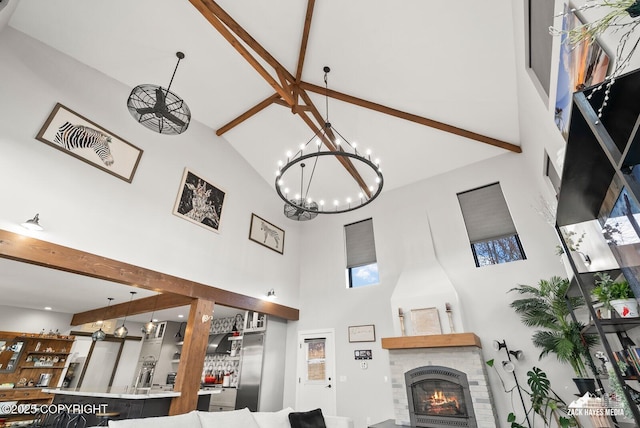 living room featuring beamed ceiling, a notable chandelier, a fireplace, and a high ceiling