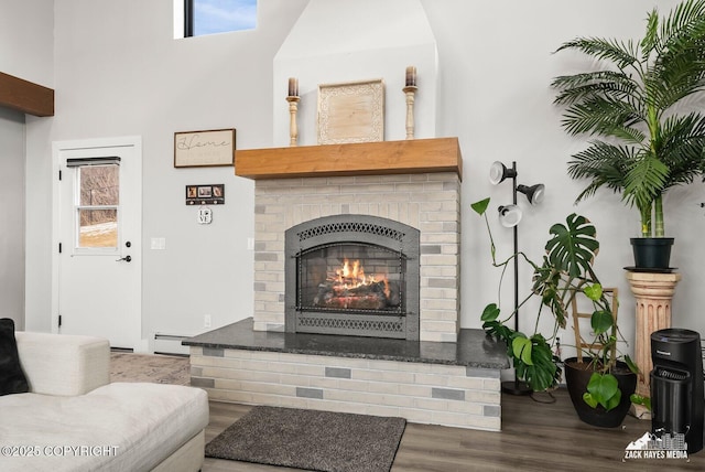 living room featuring a brick fireplace, plenty of natural light, wood finished floors, and a baseboard radiator