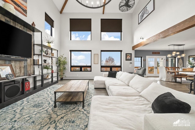 living area featuring baseboards, beam ceiling, an inviting chandelier, and wood finished floors