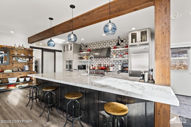 kitchen featuring a barn door, beam ceiling, premium appliances, wood finished floors, and open shelves