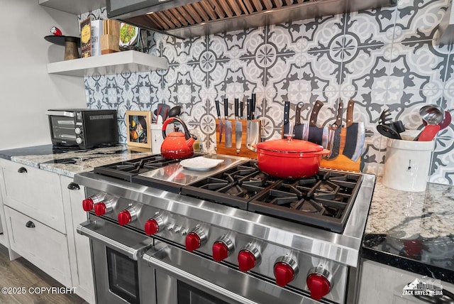 kitchen featuring backsplash, ventilation hood, range with two ovens, light stone counters, and wood finished floors