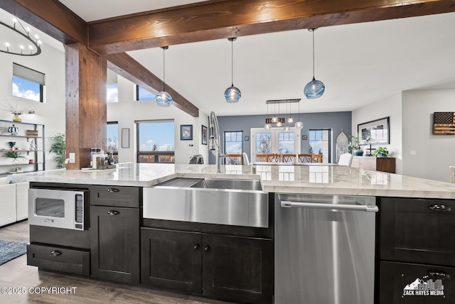 kitchen featuring beam ceiling, a sink, open floor plan, appliances with stainless steel finishes, and dark cabinets