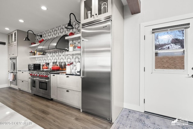 kitchen with open shelves, wood finished floors, glass insert cabinets, custom exhaust hood, and high end appliances