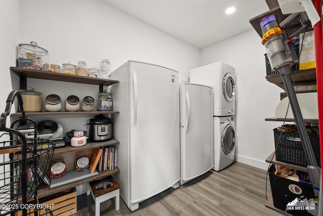 clothes washing area featuring laundry area, stacked washing maching and dryer, baseboards, and wood finished floors