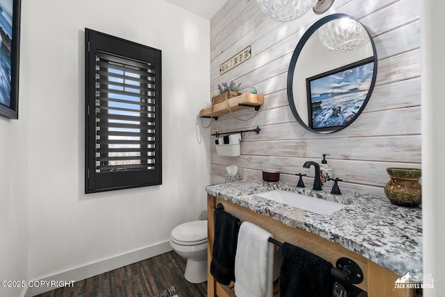 bathroom with baseboards, wood walls, toilet, wood finished floors, and vanity