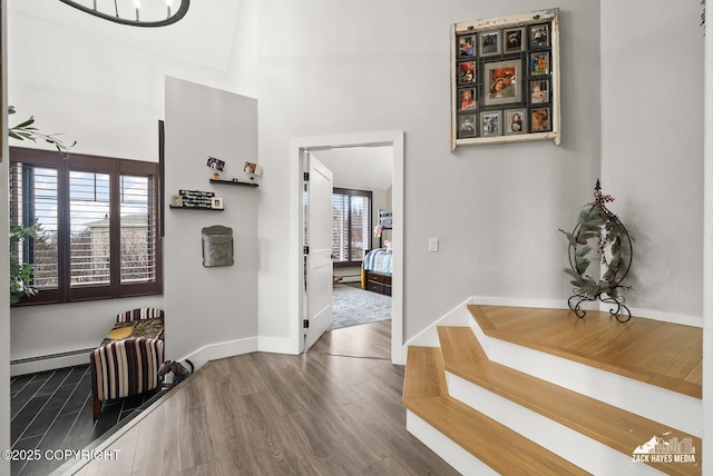 hallway featuring a baseboard heating unit, baseboards, a high ceiling, and wood finished floors