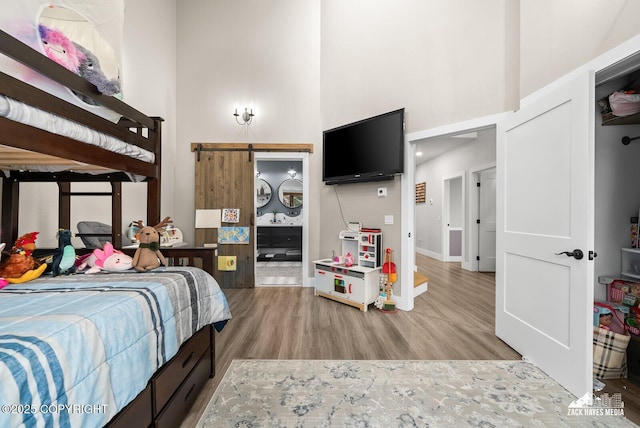 bedroom featuring a barn door, a high ceiling, baseboards, and light wood-type flooring