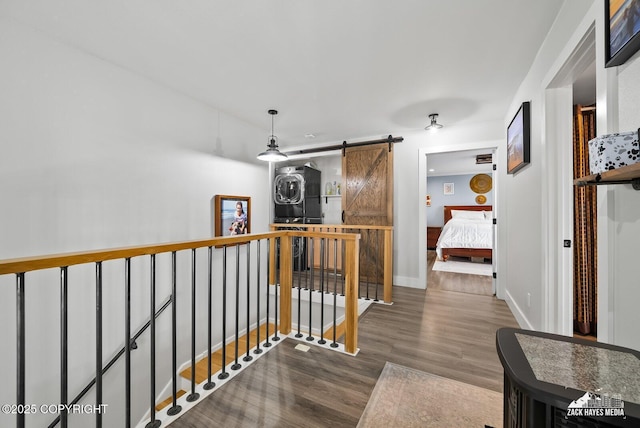 hallway featuring an upstairs landing, baseboards, a barn door, and wood finished floors