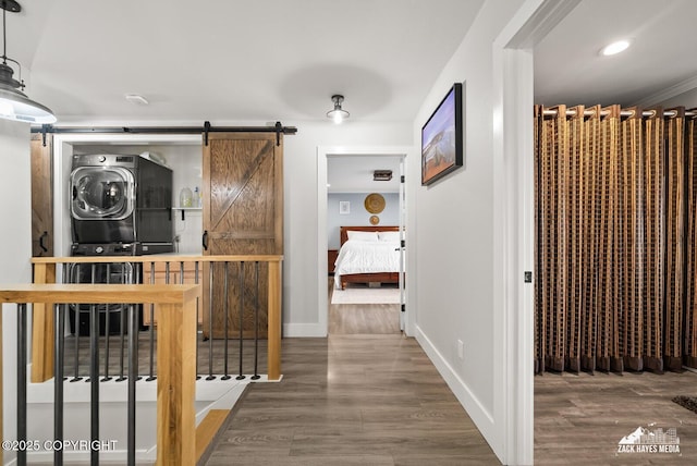 corridor featuring a barn door, wood finished floors, stacked washer / drying machine, and baseboards