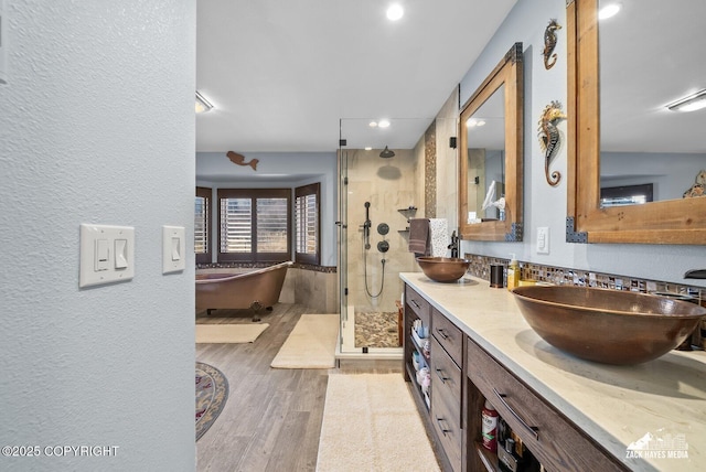 full bathroom with a stall shower, a sink, wood finished floors, double vanity, and a freestanding bath