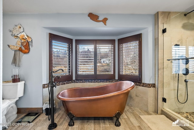 full bath with wood finish floors, a stall shower, a freestanding bath, tile walls, and toilet