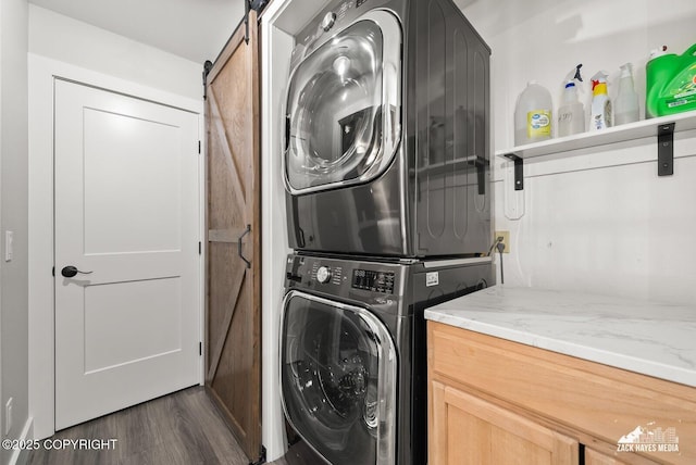 laundry room with cabinet space, dark wood-type flooring, a barn door, and stacked washer and dryer