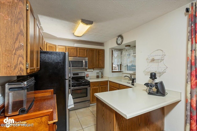 kitchen featuring light tile patterned floors, a peninsula, light countertops, appliances with stainless steel finishes, and brown cabinets