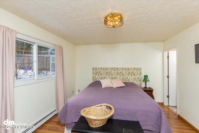 bedroom with a textured ceiling, baseboard heating, and wood finished floors