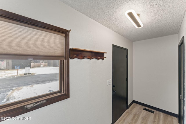 hall featuring baseboards, light wood-style flooring, visible vents, and a textured ceiling