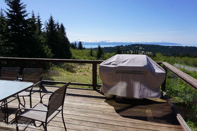 wooden terrace featuring area for grilling and a view of trees