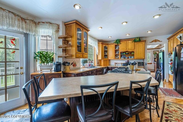 kitchen featuring light countertops, freestanding refrigerator, brown cabinets, open shelves, and glass insert cabinets