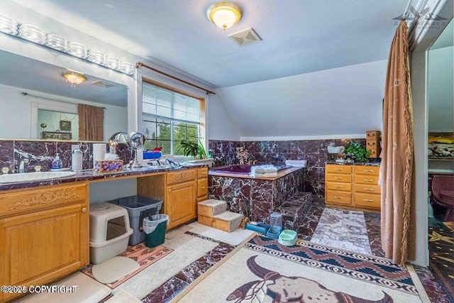 bathroom with visible vents, vanity, vaulted ceiling, tile walls, and a bath