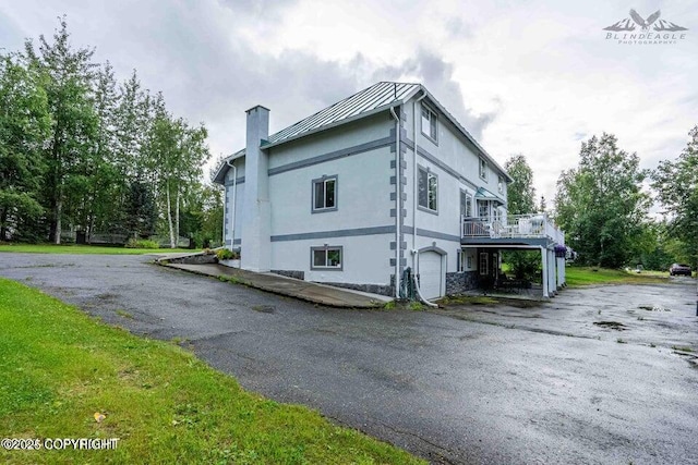 view of property exterior with driveway, a chimney, metal roof, an attached garage, and a standing seam roof