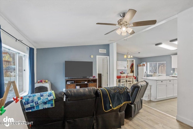 living room featuring visible vents, vaulted ceiling, light wood-style flooring, and ceiling fan with notable chandelier