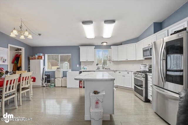 kitchen featuring light wood finished floors, a kitchen island, decorative light fixtures, stainless steel appliances, and white cabinetry