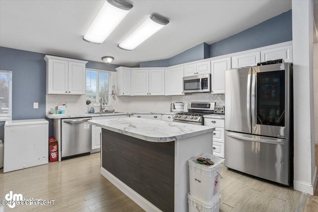 kitchen with a center island, appliances with stainless steel finishes, white cabinets, a sink, and light wood-type flooring