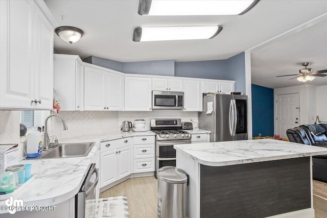 kitchen with stainless steel appliances, open floor plan, white cabinets, a sink, and light wood-type flooring