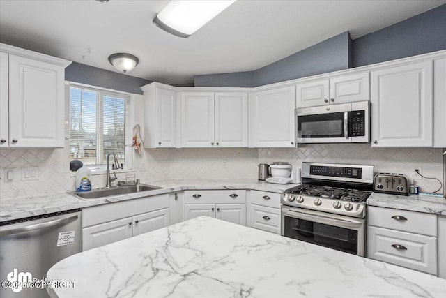 kitchen with appliances with stainless steel finishes, white cabinets, a sink, and decorative backsplash