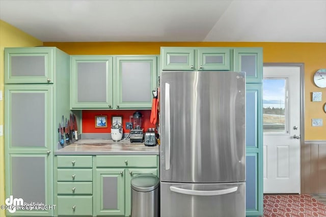 kitchen featuring a wainscoted wall, light countertops, freestanding refrigerator, and green cabinetry