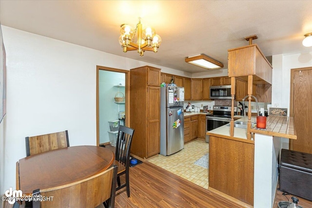 kitchen with decorative light fixtures, an inviting chandelier, appliances with stainless steel finishes, brown cabinetry, and a peninsula