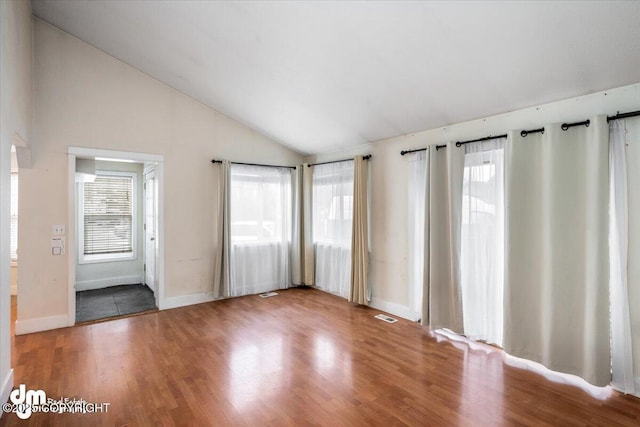 spare room featuring vaulted ceiling, wood finished floors, and a healthy amount of sunlight