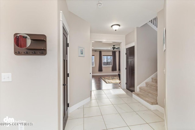 hallway featuring light tile patterned floors, baseboards, and stairway