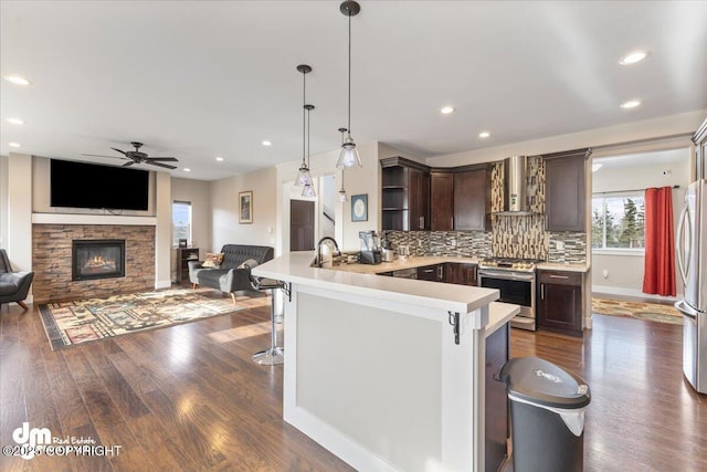 kitchen featuring stainless steel appliances, a peninsula, open shelves, light countertops, and wall chimney exhaust hood