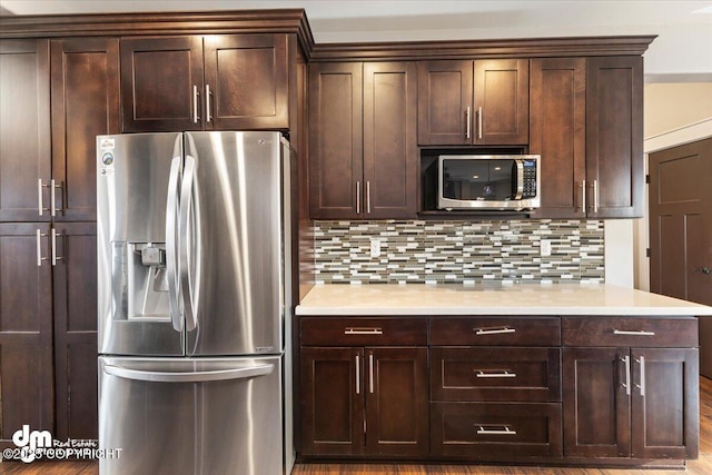 kitchen with appliances with stainless steel finishes, light countertops, dark brown cabinetry, and backsplash