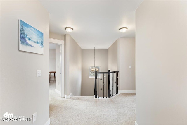 hall featuring a chandelier, baseboards, carpet flooring, and an upstairs landing