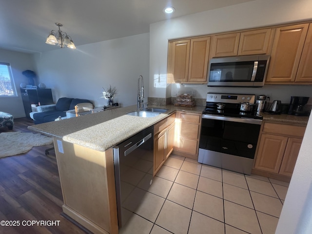 kitchen with a peninsula, a sink, open floor plan, appliances with stainless steel finishes, and decorative light fixtures