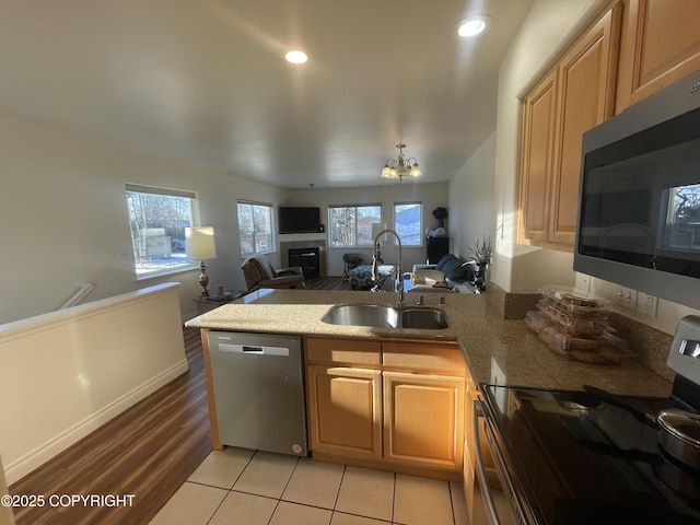 kitchen with appliances with stainless steel finishes, a glass covered fireplace, open floor plan, a sink, and a peninsula