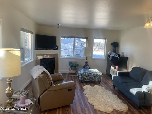 living area featuring dark wood-style floors, a glass covered fireplace, and baseboards