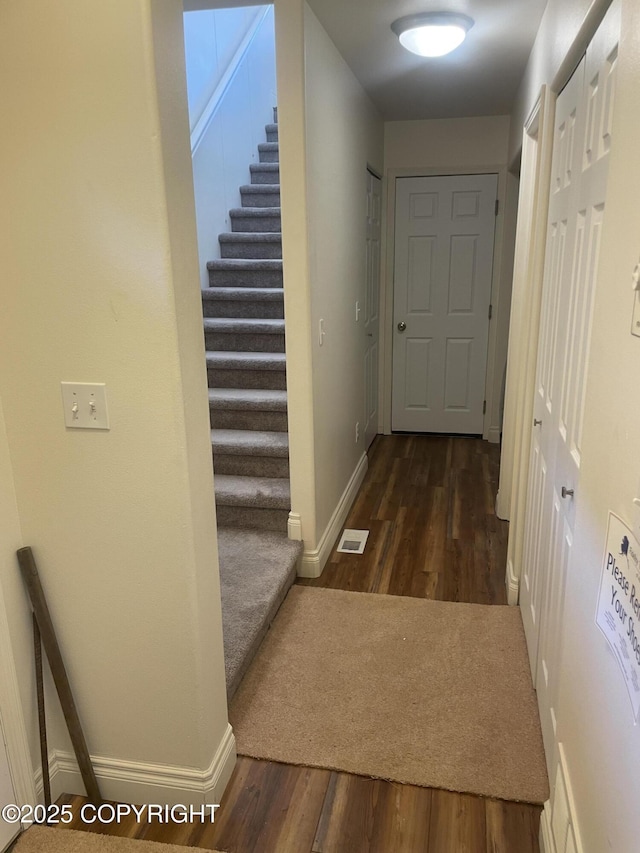 hallway with dark wood finished floors, baseboards, and stairs