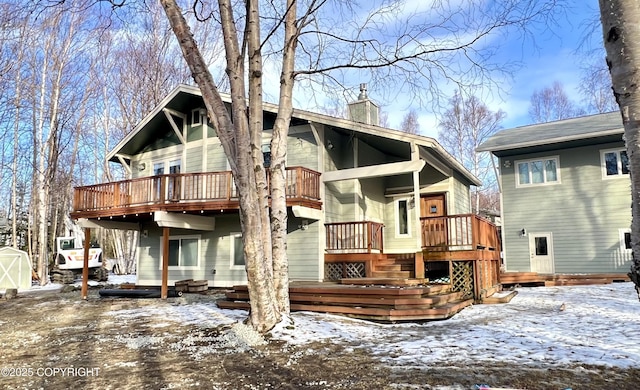 snow covered property featuring a chimney, an outbuilding, and a wooden deck