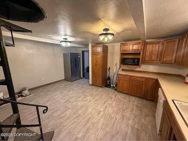 kitchen with brown cabinetry, a textured ceiling, light countertops, and black microwave