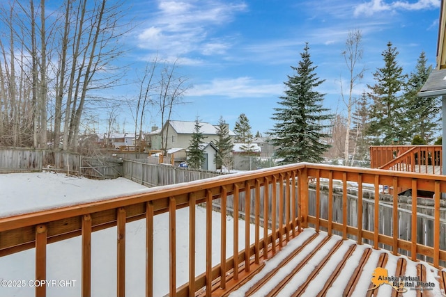 snow covered deck with a fenced backyard