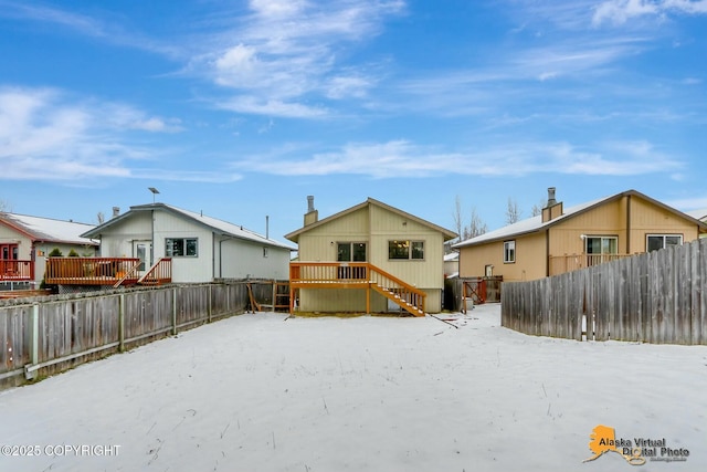 snow covered back of property with a fenced backyard and a wooden deck