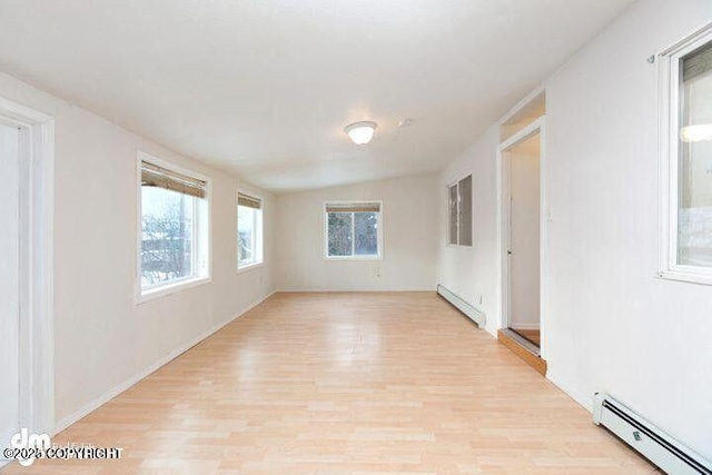 unfurnished room featuring a baseboard heating unit, lofted ceiling, and light wood-style floors