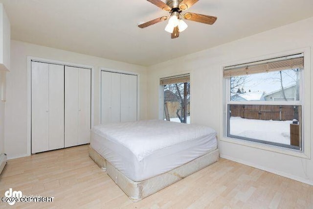 bedroom with baseboards, two closets, light wood-style flooring, and a ceiling fan