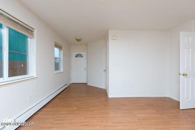 empty room with a baseboard heating unit, light wood-style flooring, and baseboards