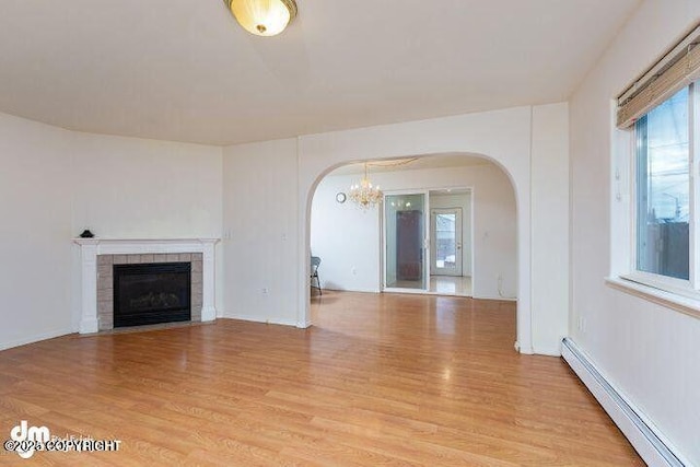 unfurnished living room featuring arched walkways, baseboard heating, a tiled fireplace, and light wood-style floors