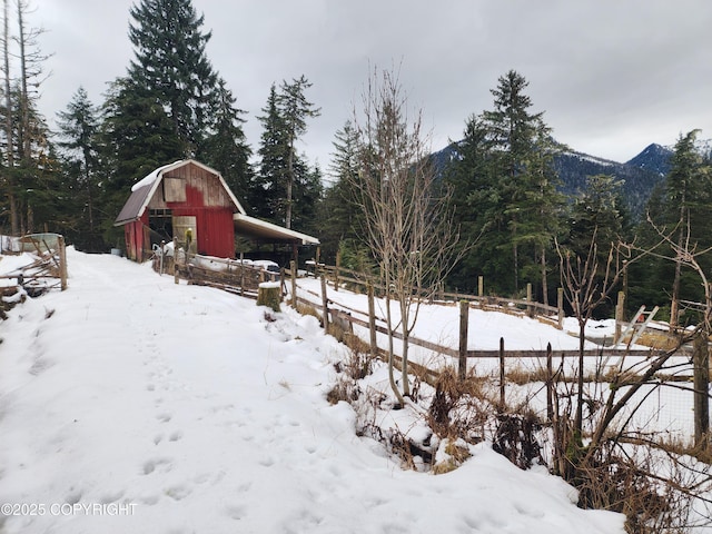 yard covered in snow featuring a barn, fence, a mountain view, and an outbuilding