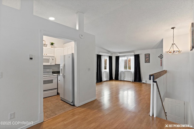 kitchen with white appliances, a textured ceiling, light wood finished floors, and white cabinets