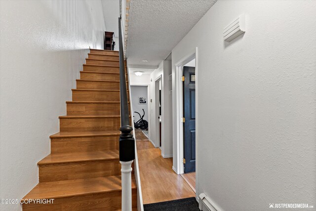 stairs with a textured ceiling, a textured wall, and wood finished floors